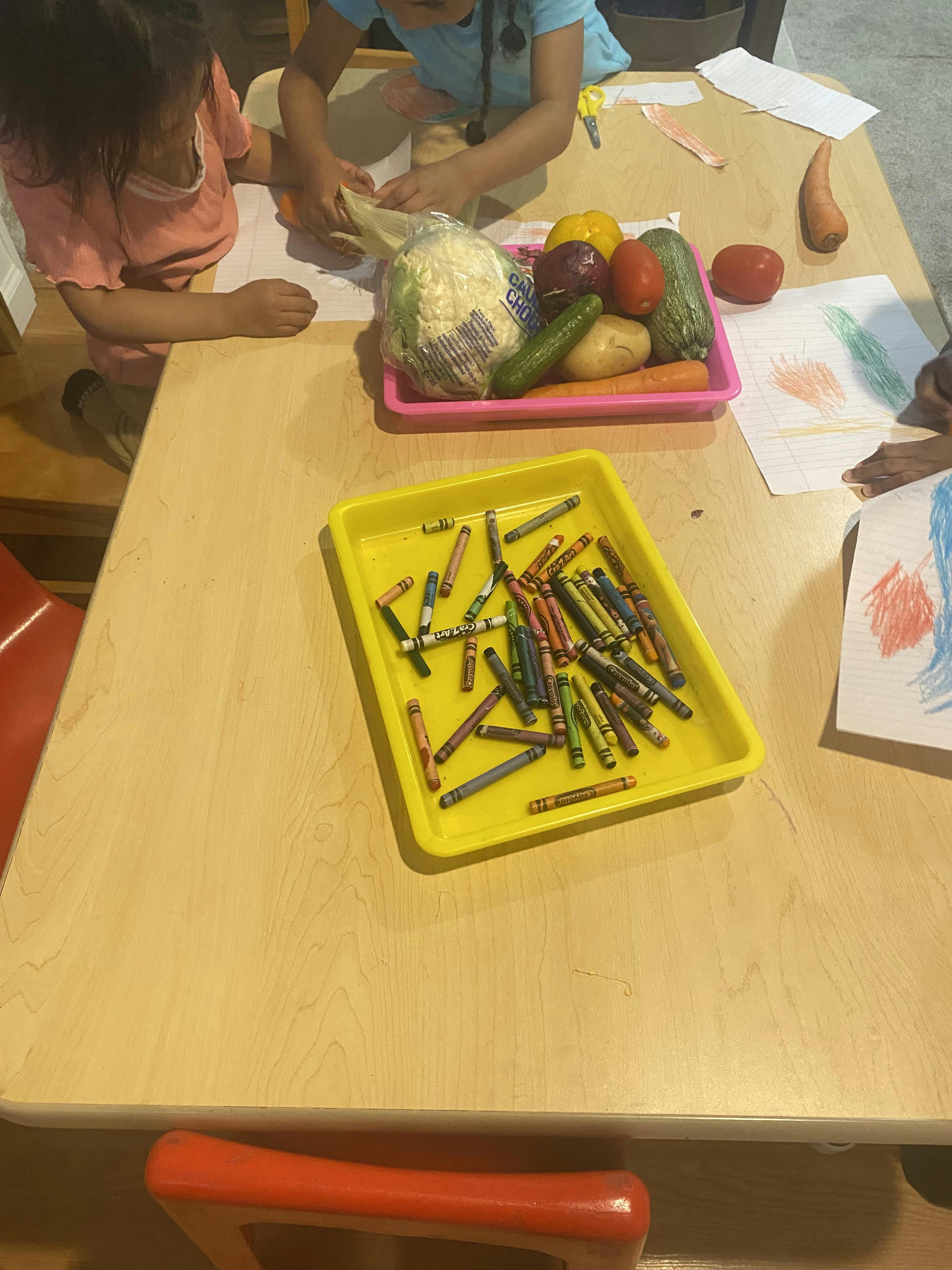 Children at a table with crayons and a tray of vegetables