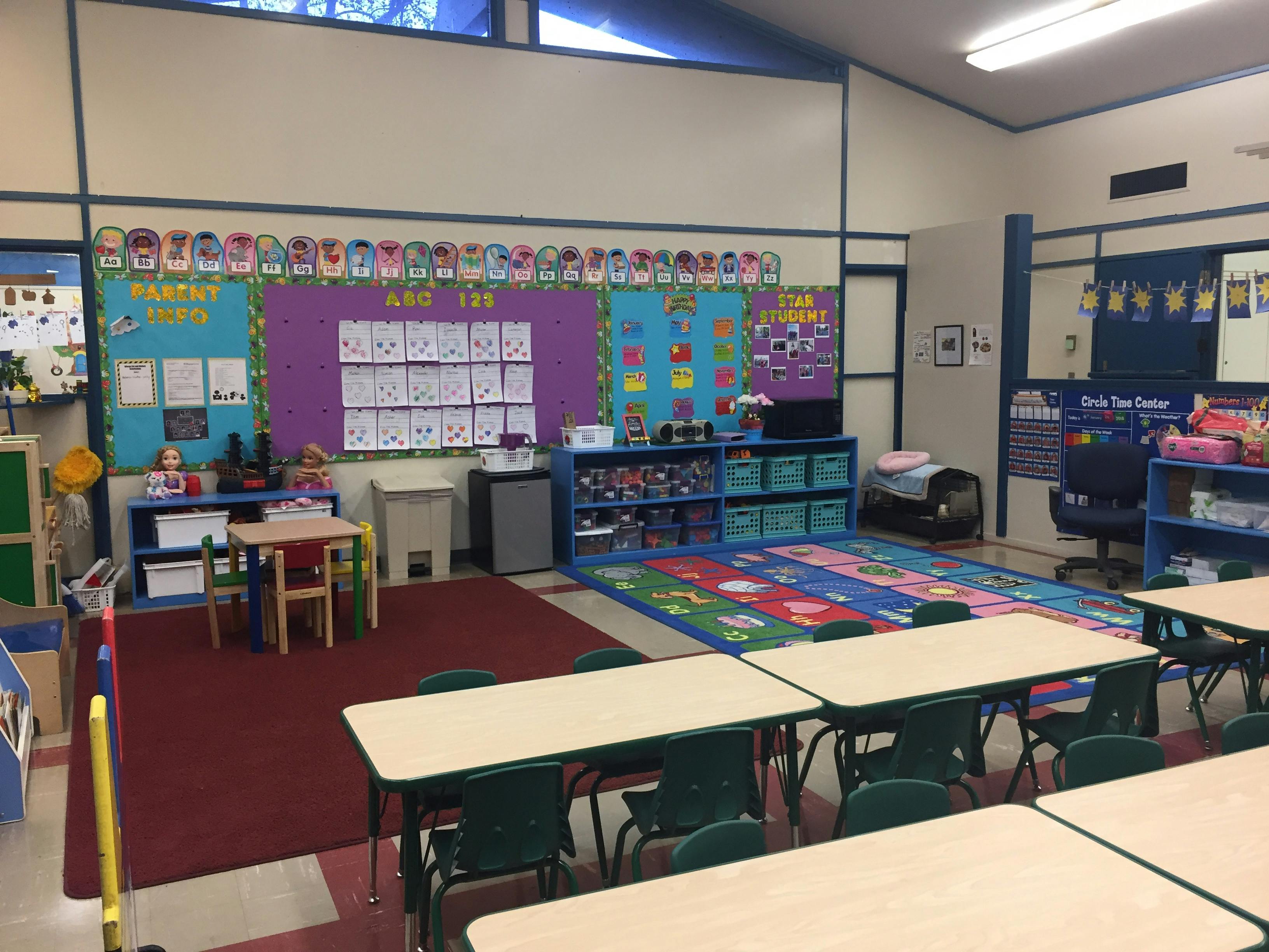 Classroom with small tables and chairs, colorful rugs, and bulletin boards