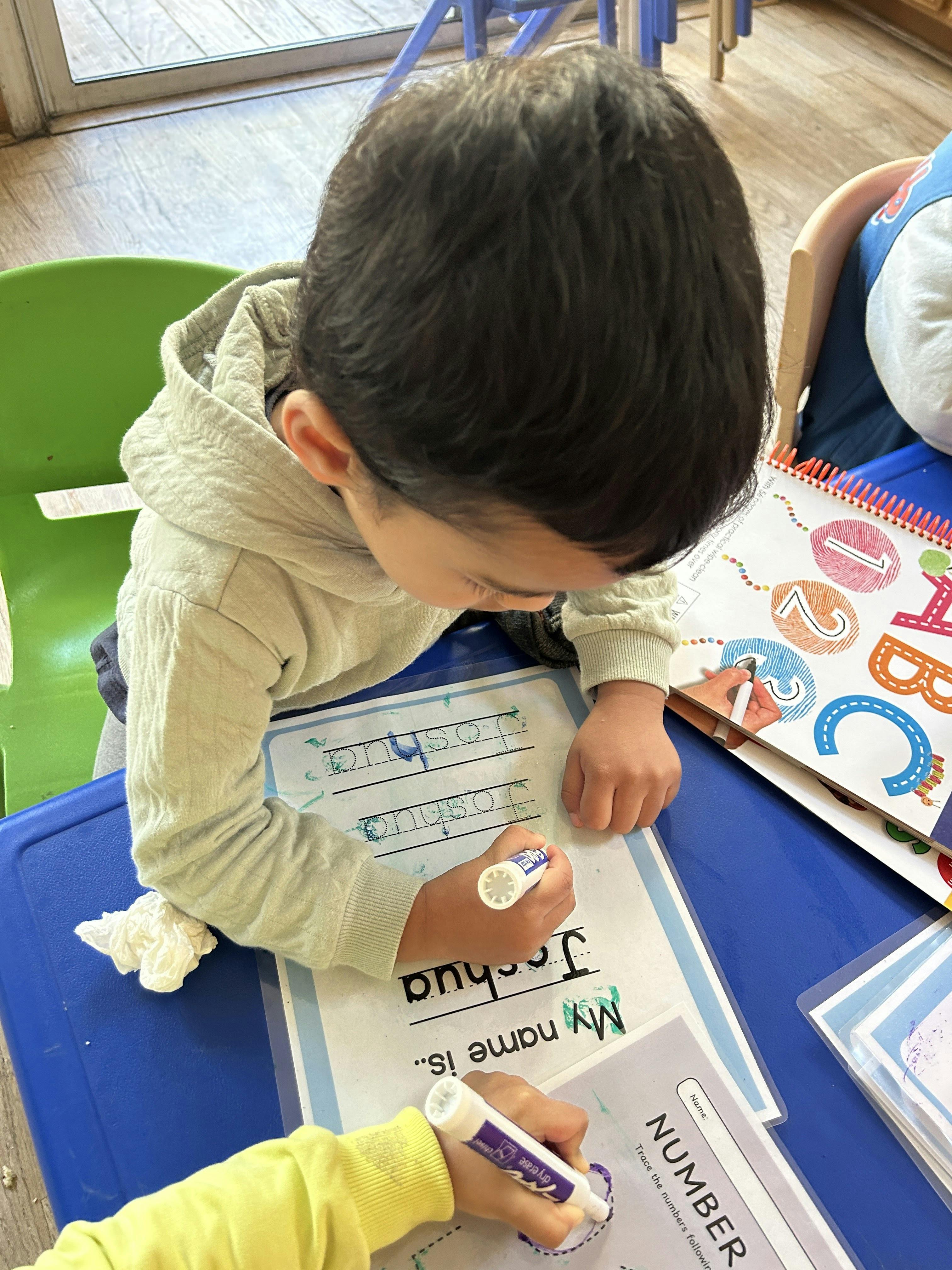 Child tracing the name \"Joshua\" and \"NUMBER\" on activity sheets
