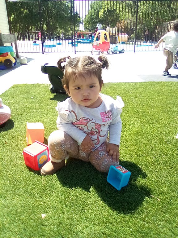 Child kneeling on grass with blocks