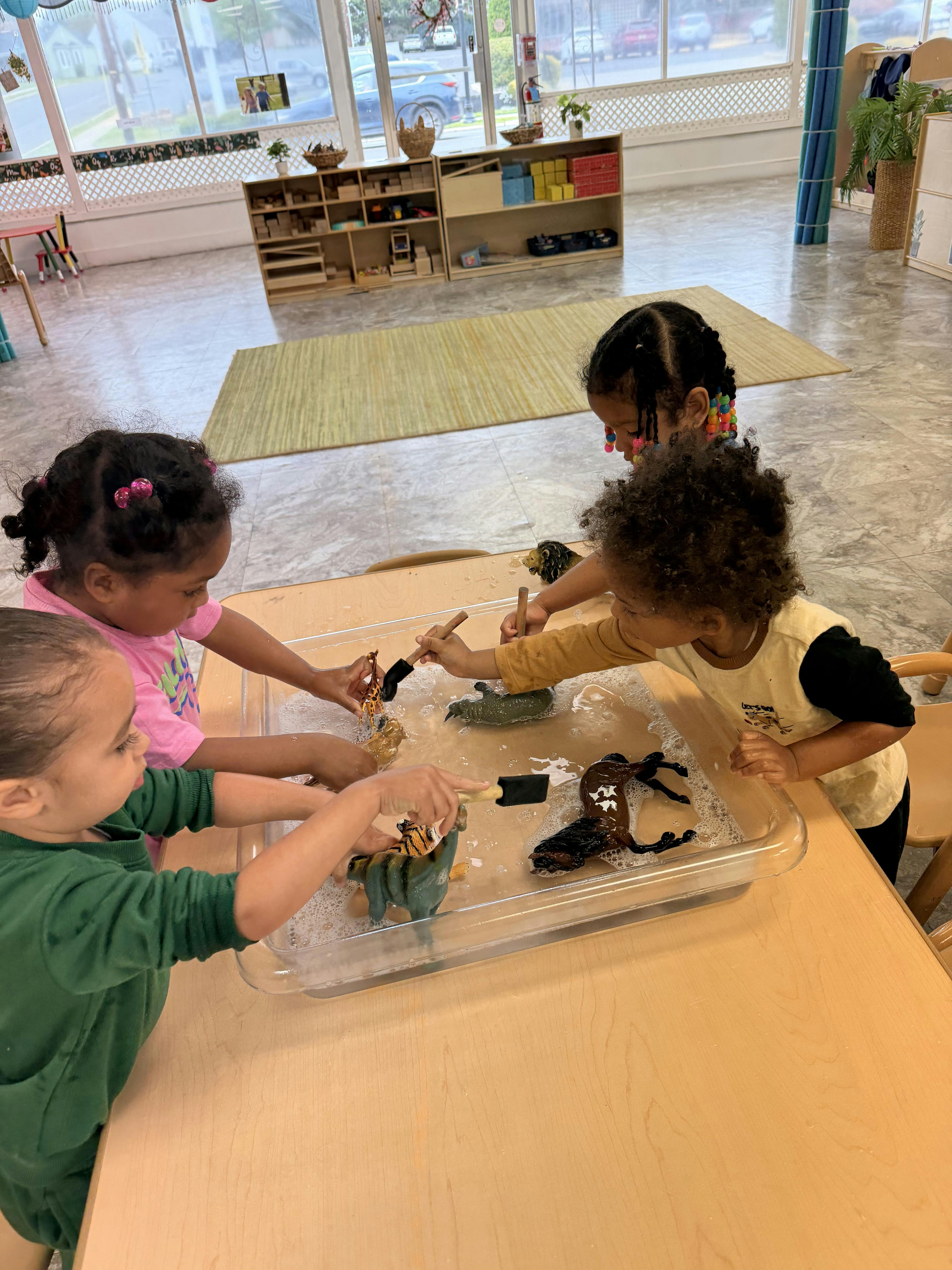 Four children playing with animal figurines in bubbly water