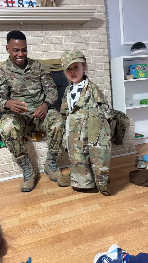 Person in military uniform sitting while a child wears an oversized uniform jacket