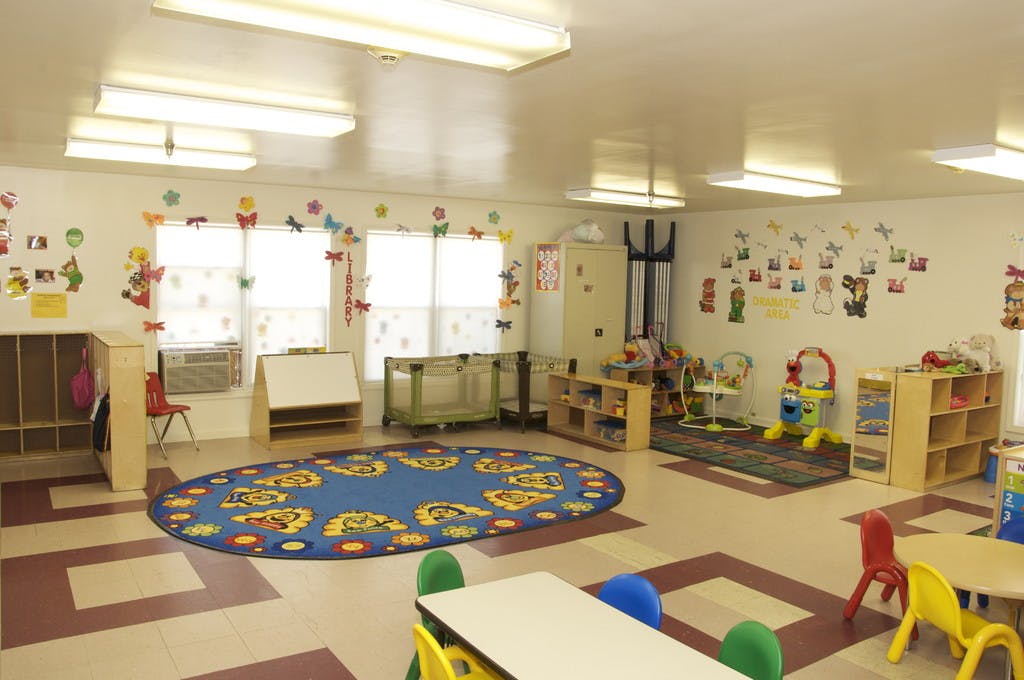 Empty classroom with small tables, chairs, and a blue oval rug