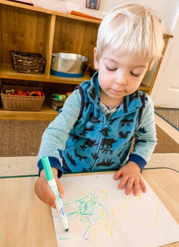 Child drawing on paper with a green marker