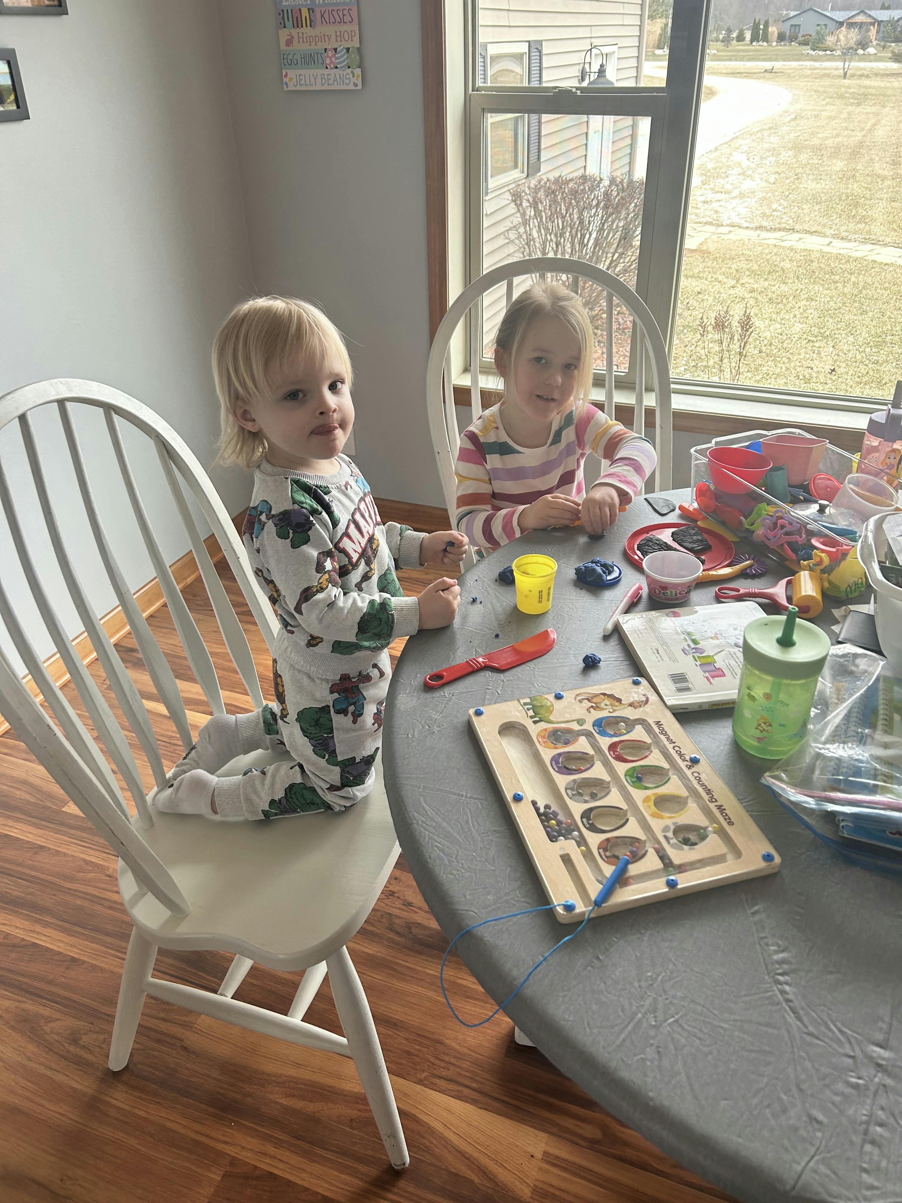 Two children at a table playing with modeling clay and toys