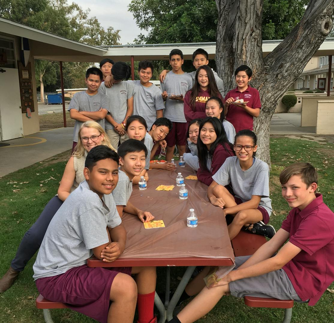Group of teens and an adult gathered around a picnic table outdoors