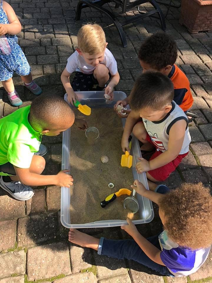 Children playing with sand and toys in a plastic bin outdoors