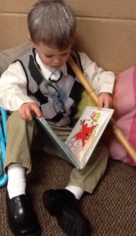 Child in a sweater vest and tie reading a book