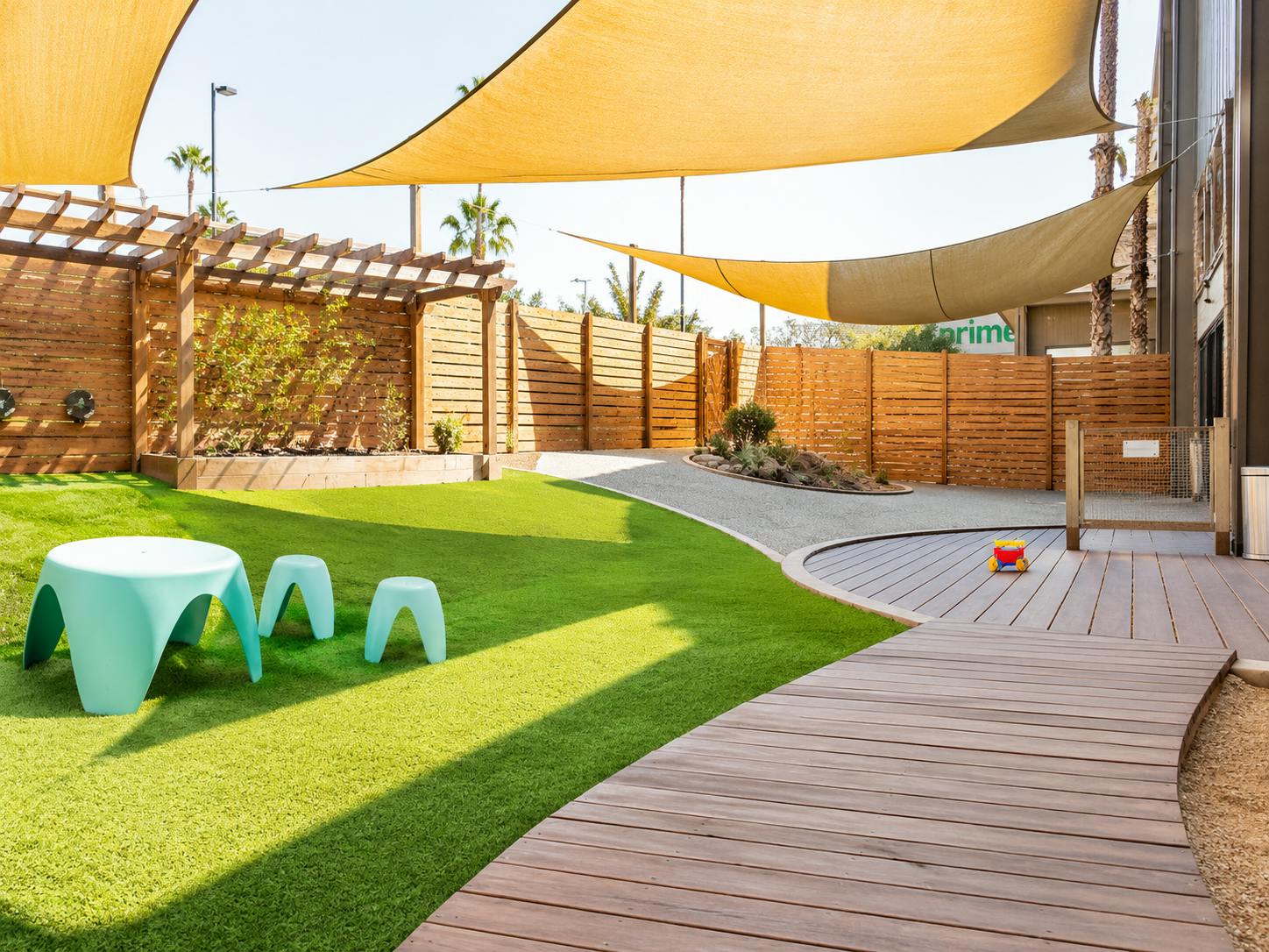 Outdoor children play area with artificial turf, wooden fencing, and shade sails