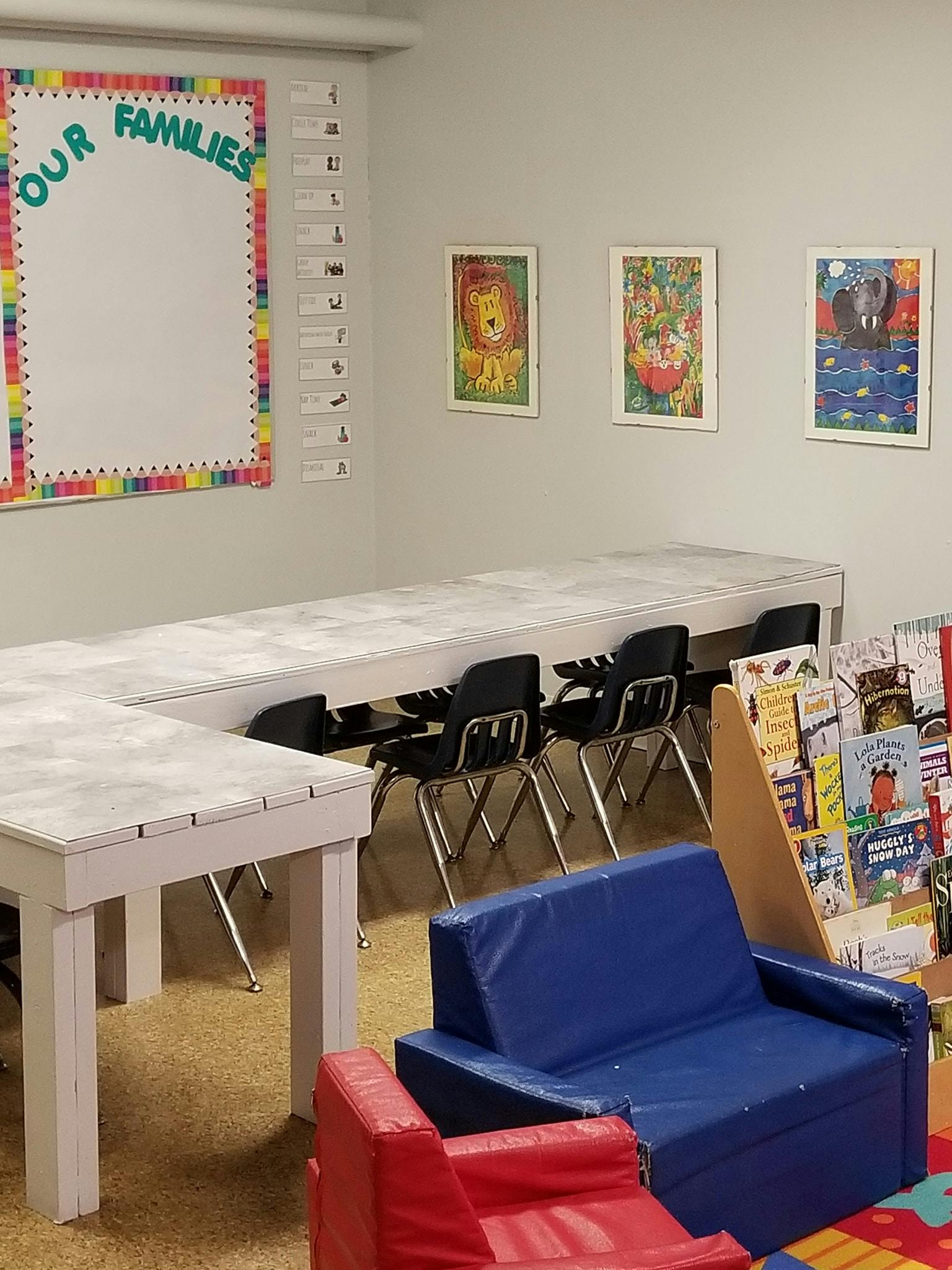 Classroom with tables, chairs, a whiteboard with "OUR FAMILIES" and children's books