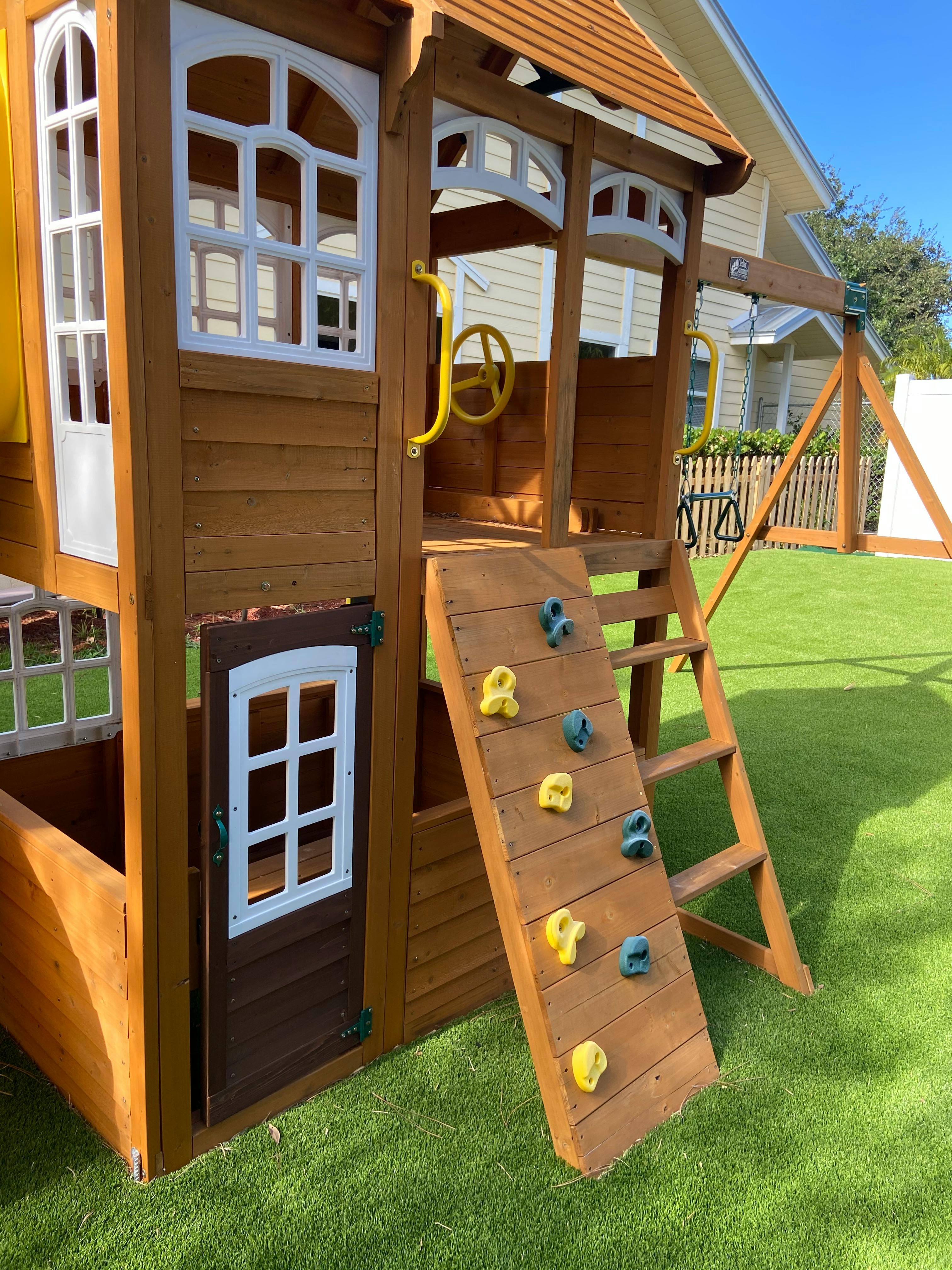 Wooden playhouse with a ladder and rock climbing wall