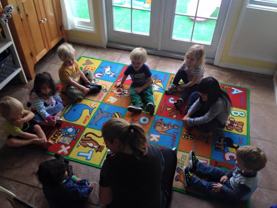 Adult and children sitting on a colorful alphabet rug
