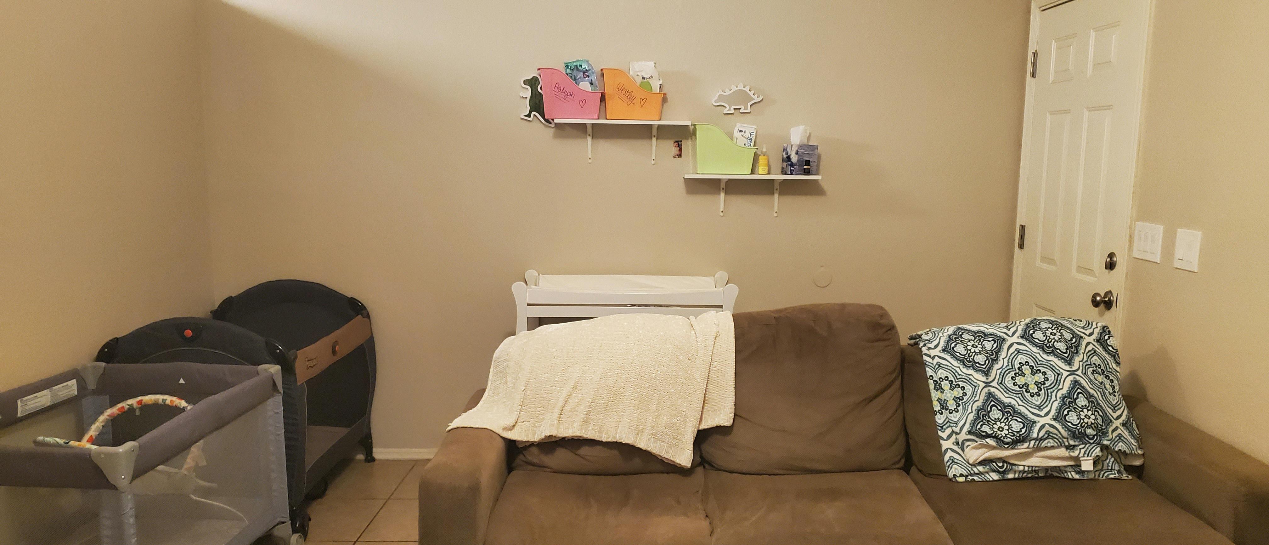 Living room with a brown couch, baby bassinet, and shelves on the wall