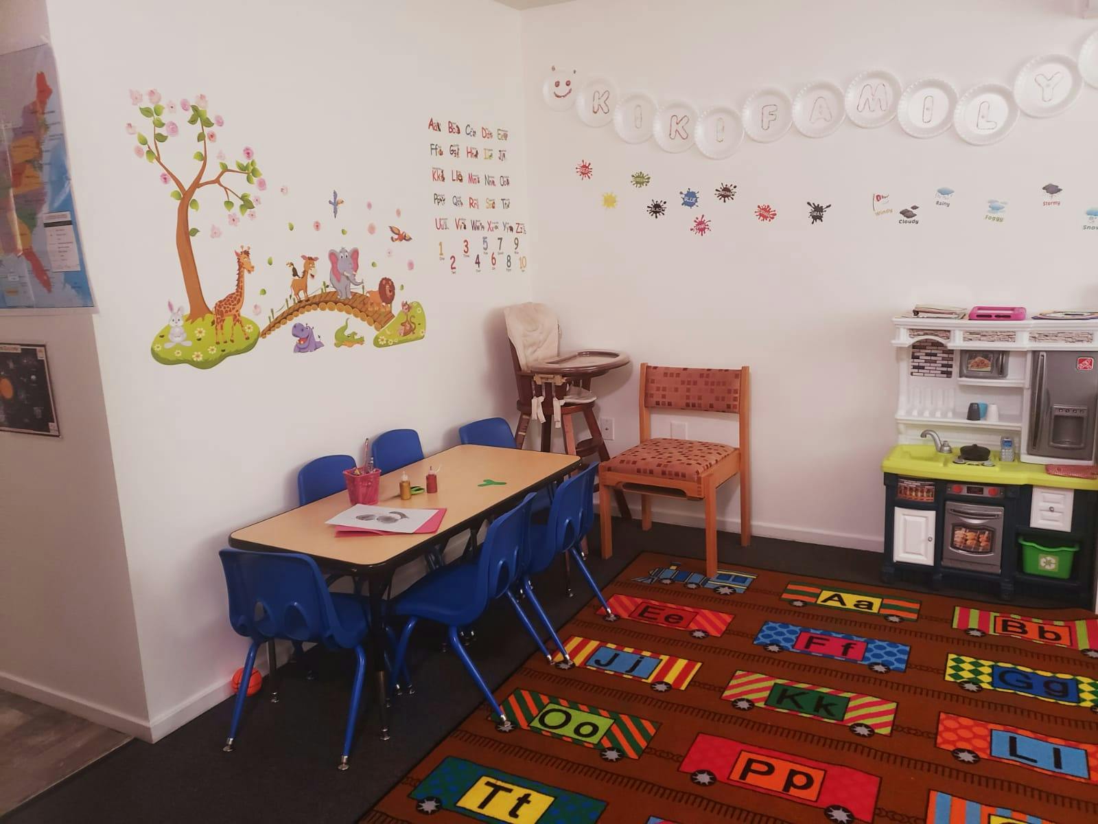 Children's classroom with small tables and chairs, play kitchen, and alphabet rug