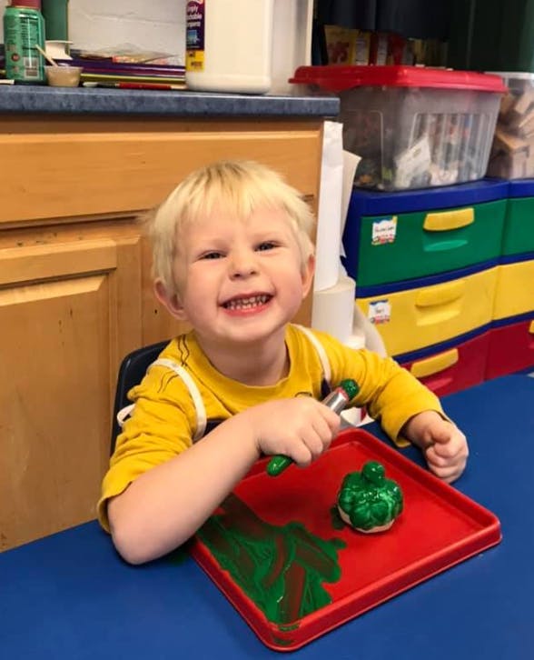 Child painting a green object on a red tray