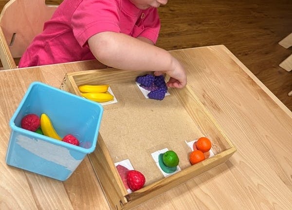 Child sorting toy fruit in a wooden tray on a table