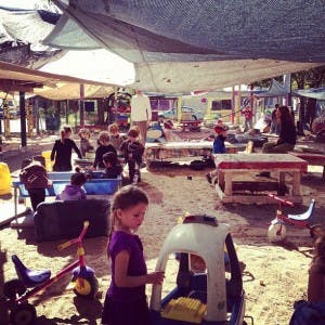 Children playing in a shaded outdoor area with toys and tables