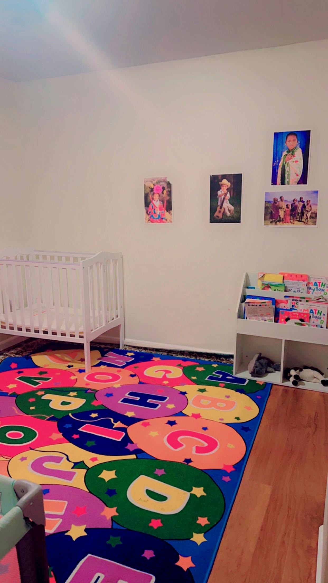 Nursery room with a white crib, colorful alphabet rug, and bookshelf