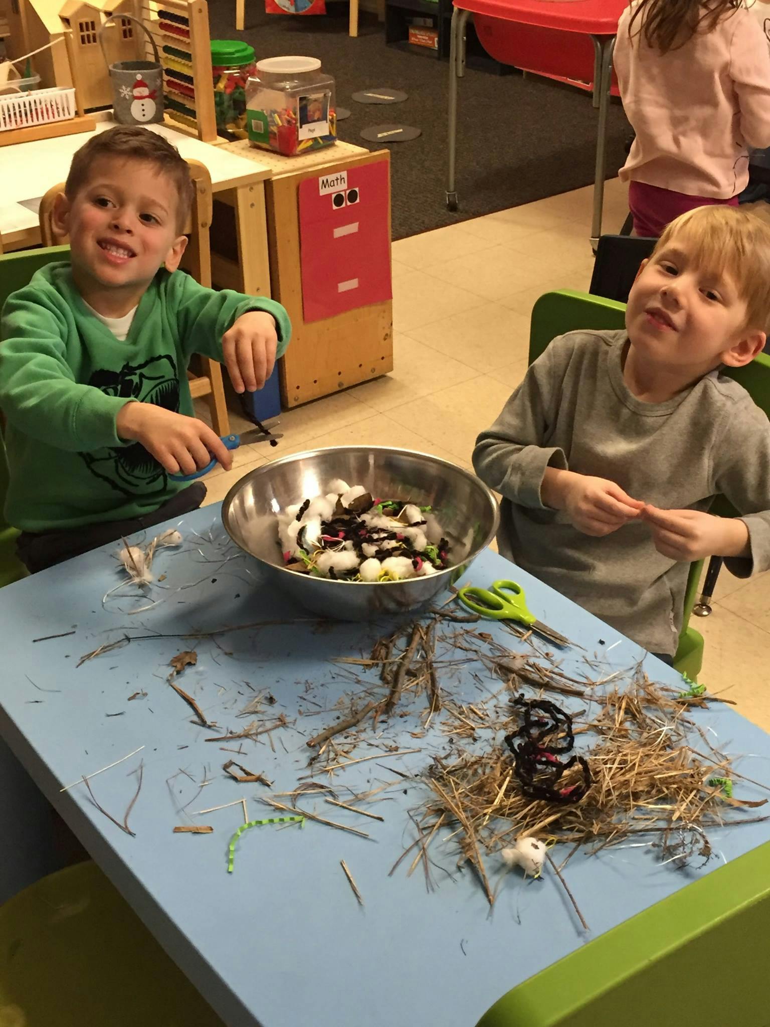 Two children at a table with a bowl of beans and craft materials