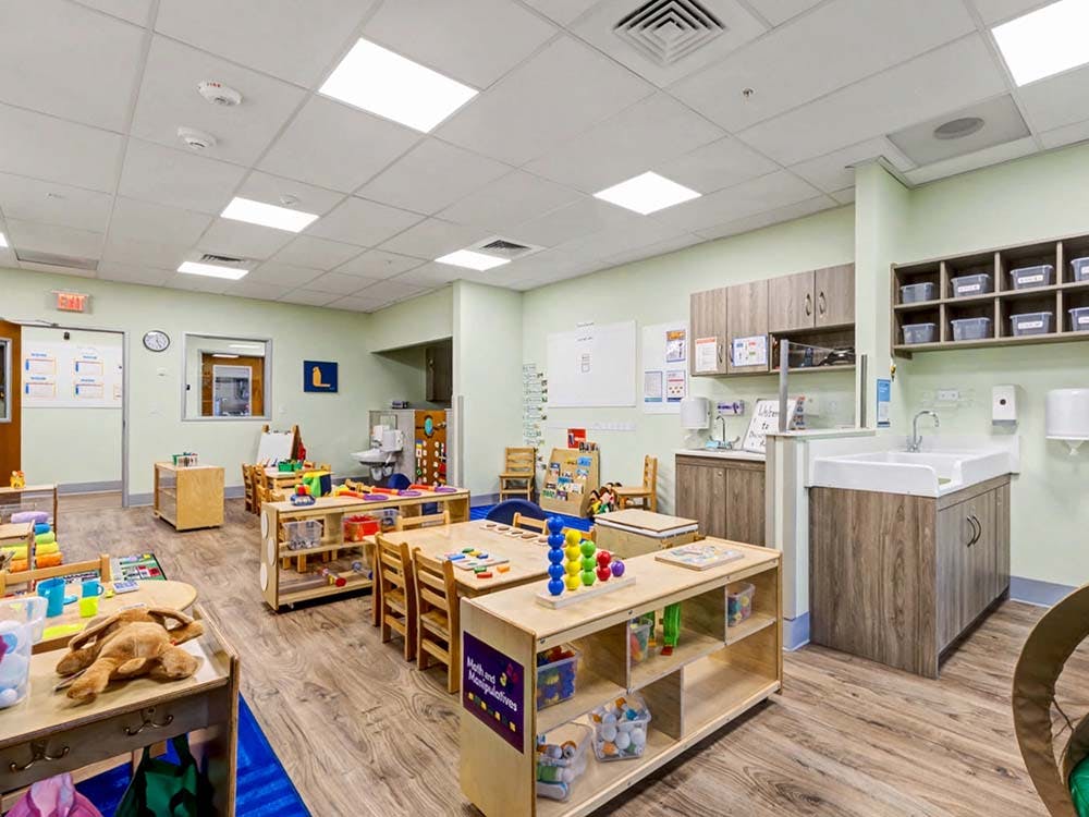 A colorful empty classroom with many toys, small tables, chairs, and sinks