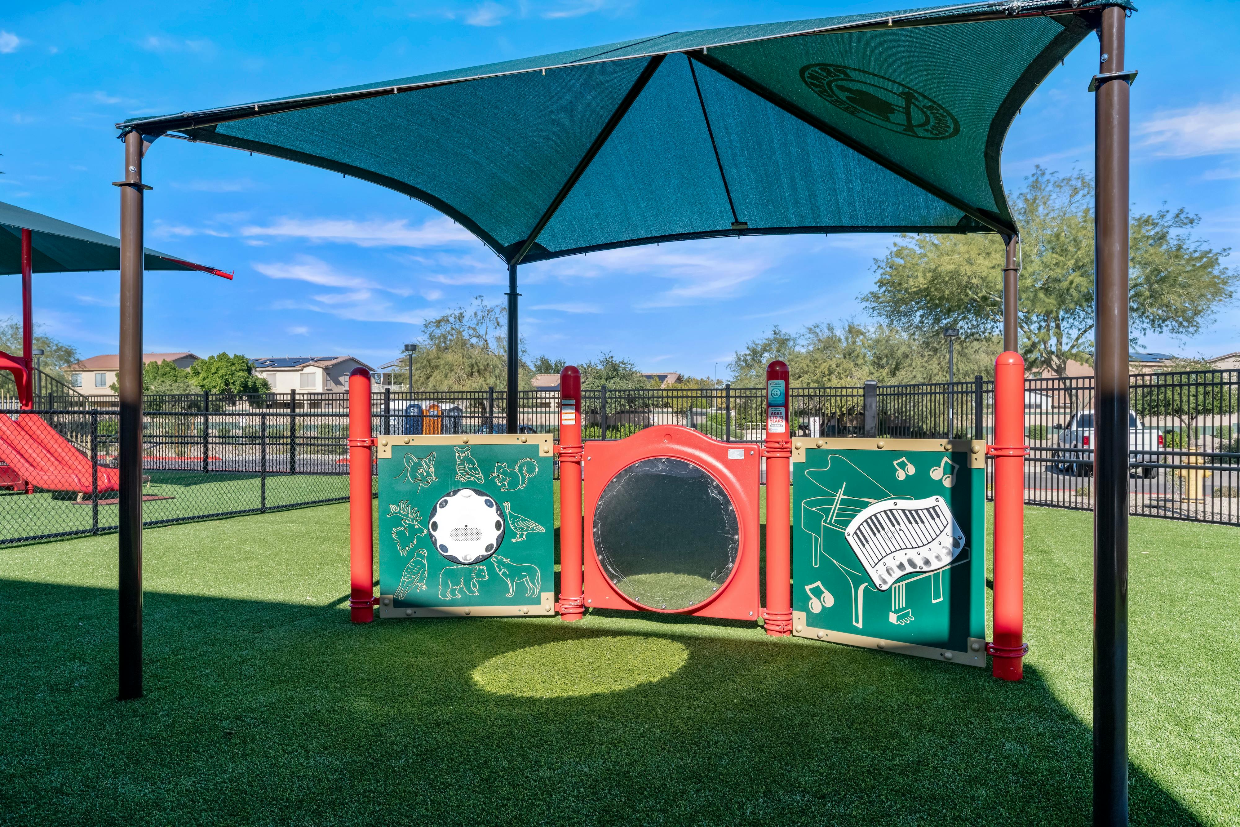 Playground equipment with shade canopy, fenced artificial turf, and play panels
