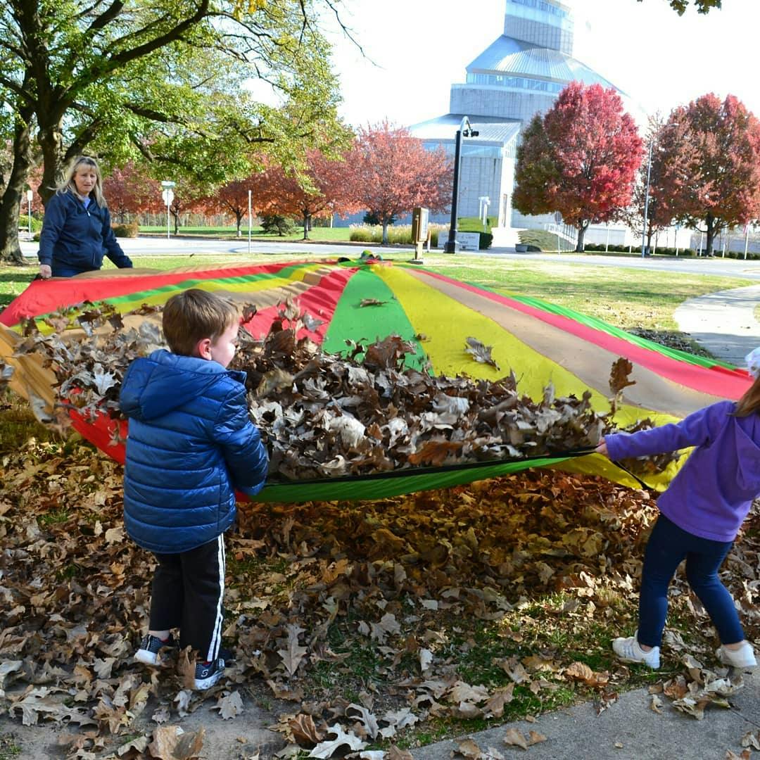 Two children and an adult moving a colorful tarp full of leaves