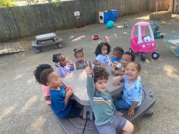 Group of children seated around a small outdoor picnic table