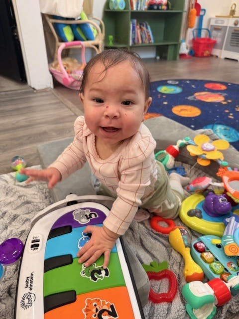 Child on a gray blanket playing with an "Baby Einstein" musical toy