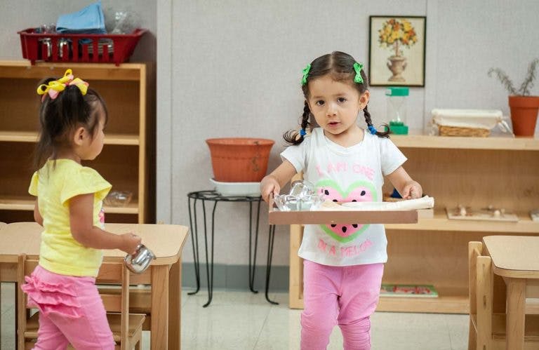 Child carrying a tray with small items in a classroom