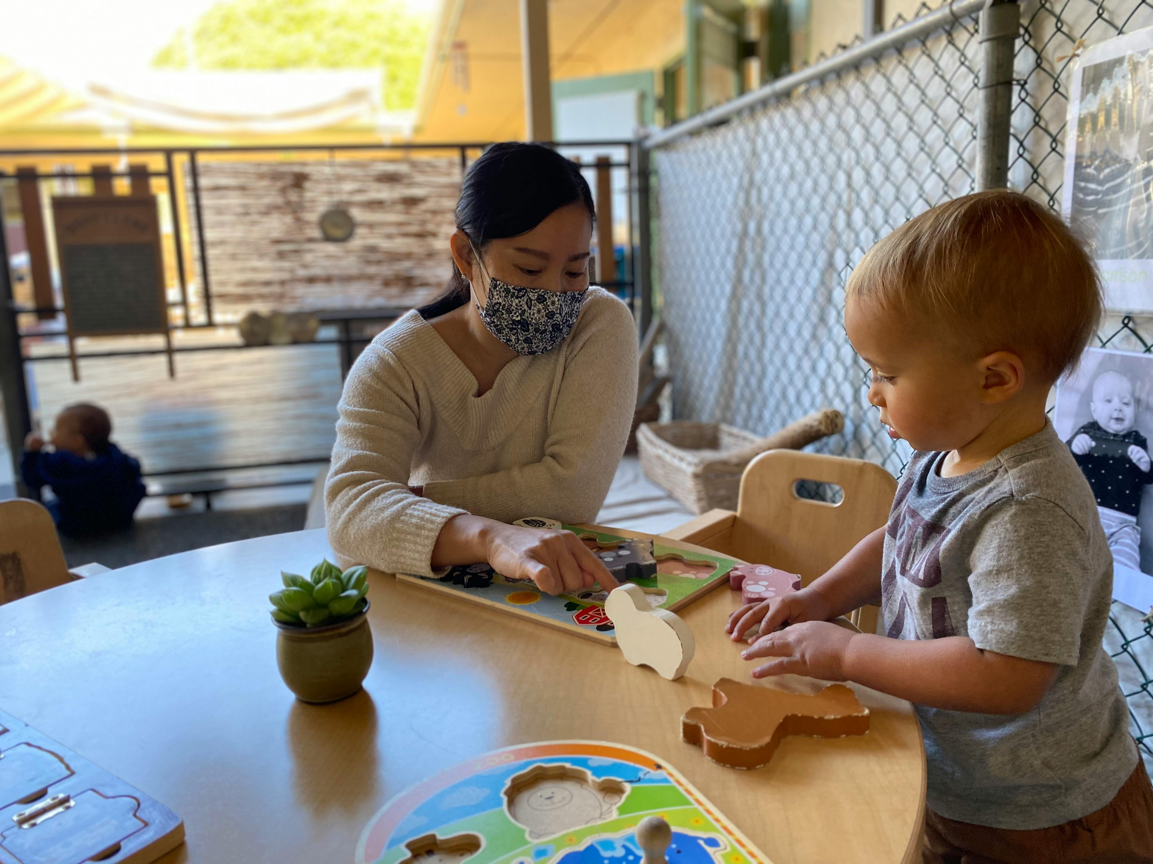 Person in mask and child playing with puzzles at a table