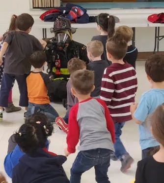 Person in firefighter gear surrounded by children