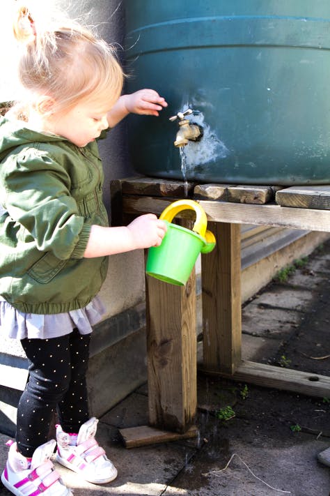 Child filling a watering can from a spigot on a large barrel