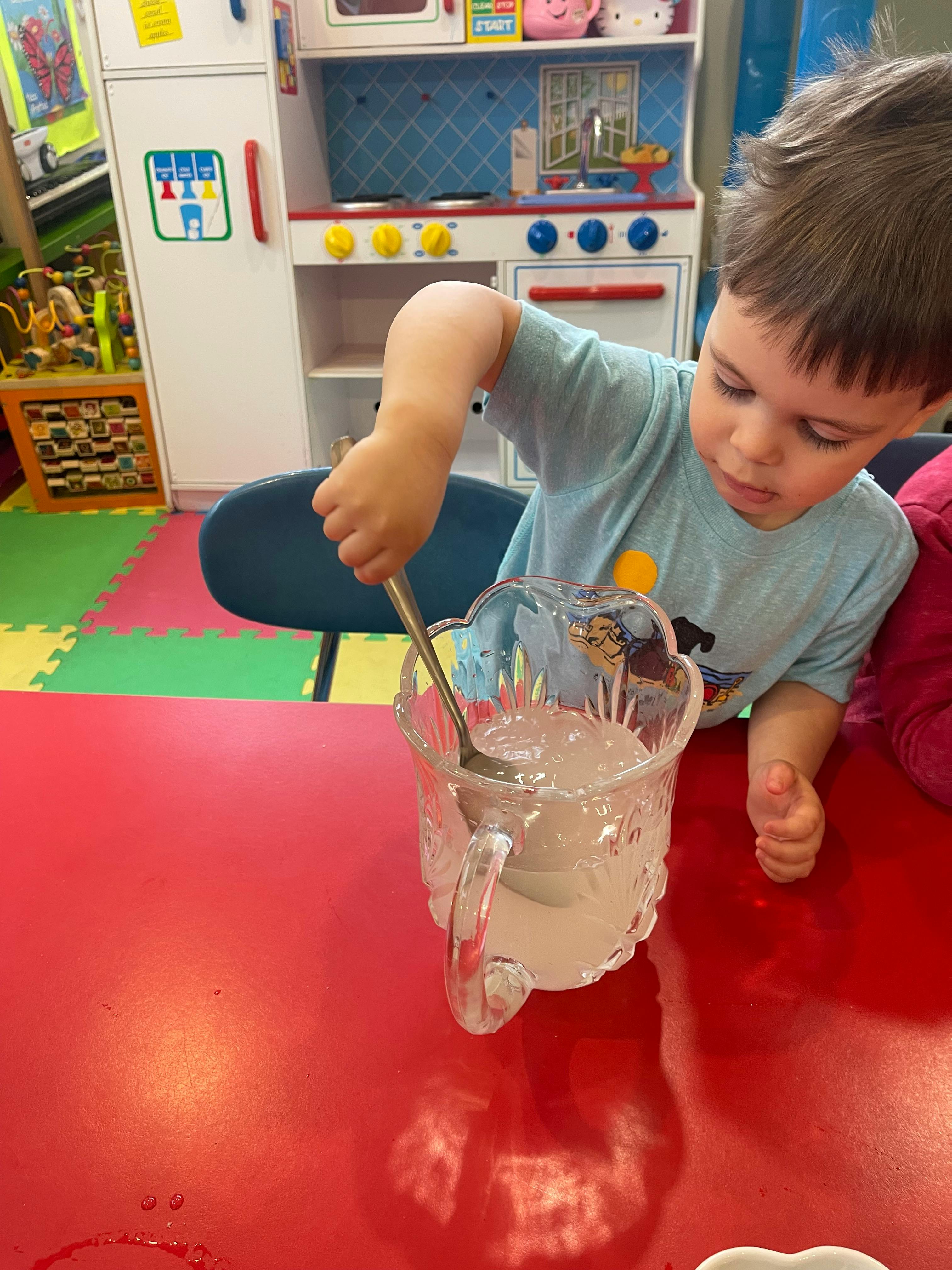 Child stirring liquid in a pitcher with a spoon