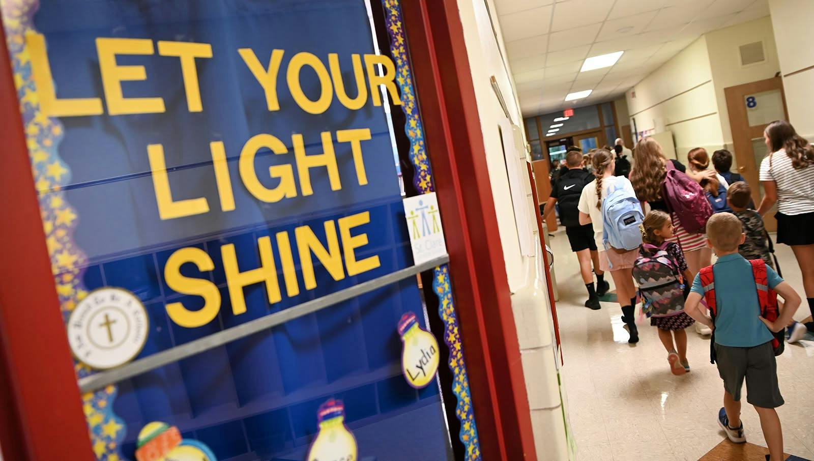 Students walking down a school hallway past a door with Let Your Light Shine text