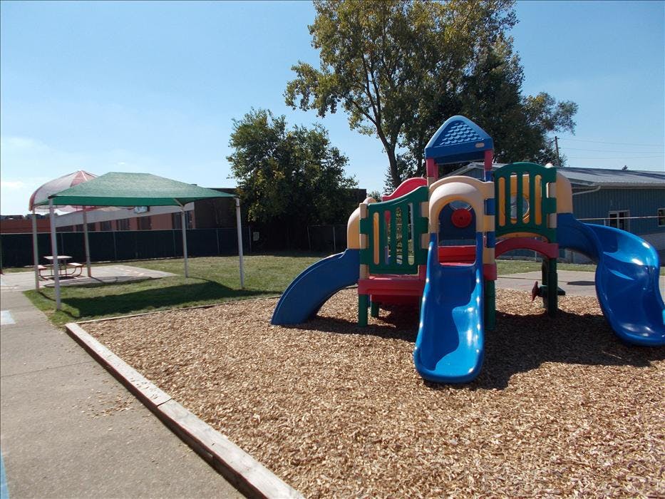 Colorful playground structure with slides on wood chips next to a green canopy and picnic table