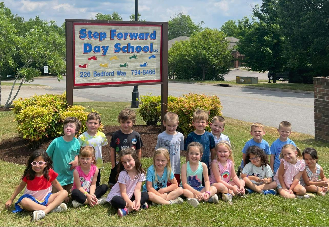 Group of children sitting and standing in front of a sign for Step Forward Day School