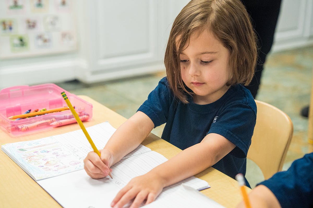 Child writing with a pencil at a desk in a classroom