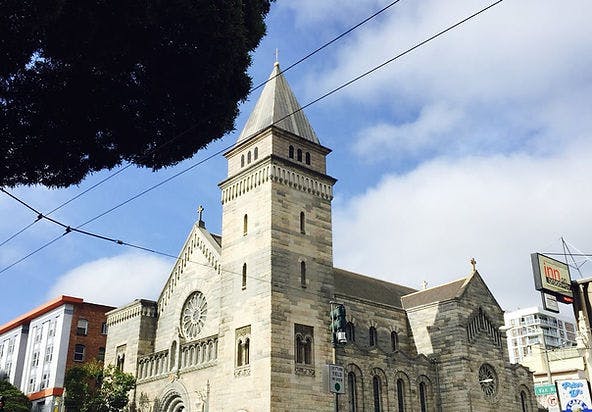 Stone church with a tall steeple against a blue sky with white clouds