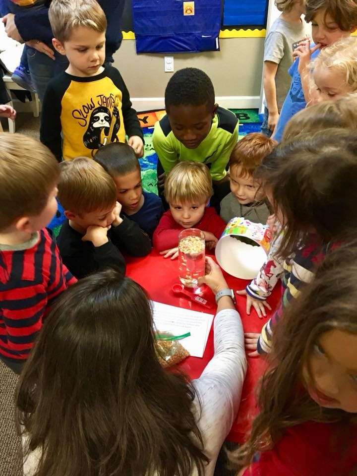 Children gathered around a table looking at a glass jar held by an adult