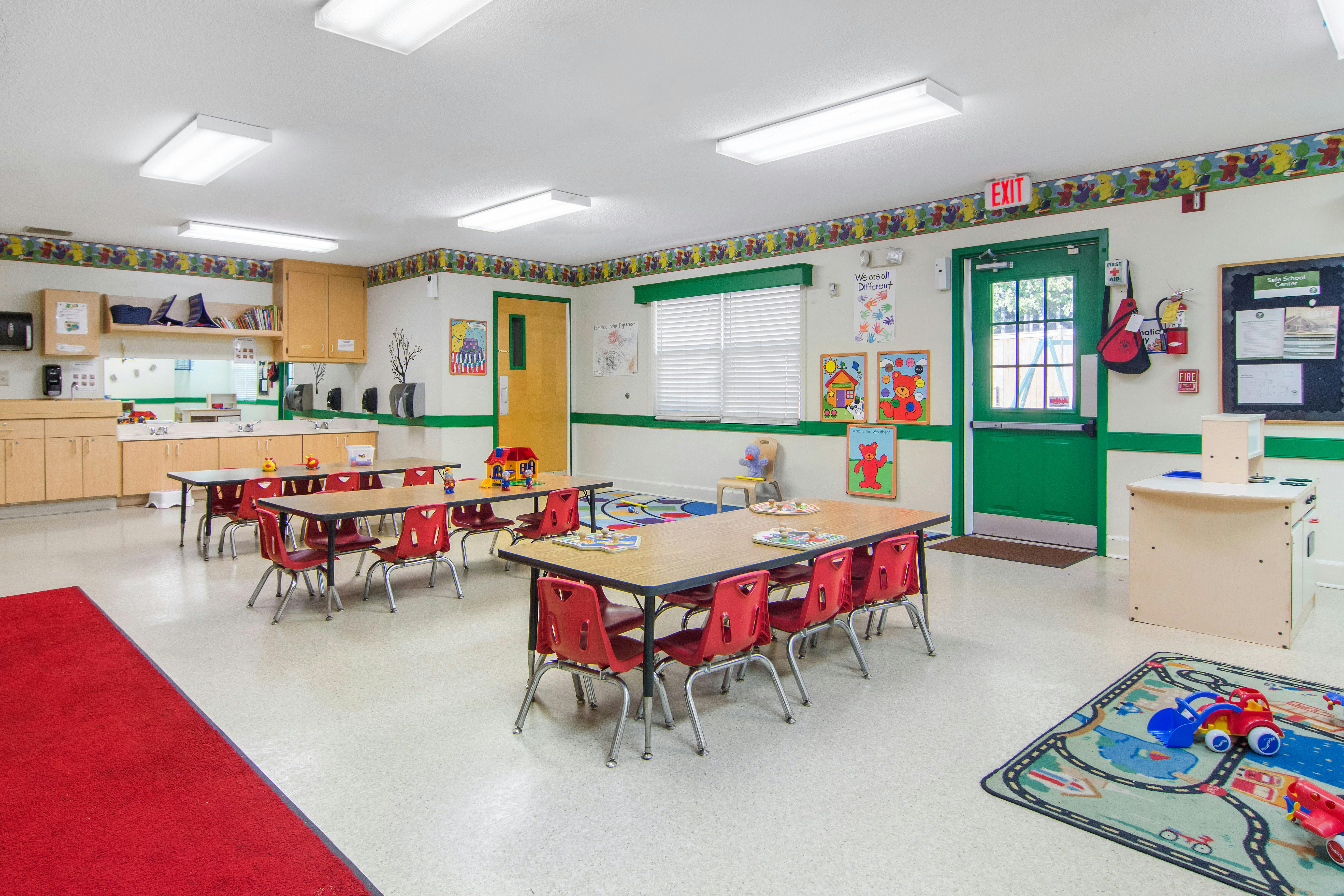 An empty early childhood classroom with small tables and red chairs