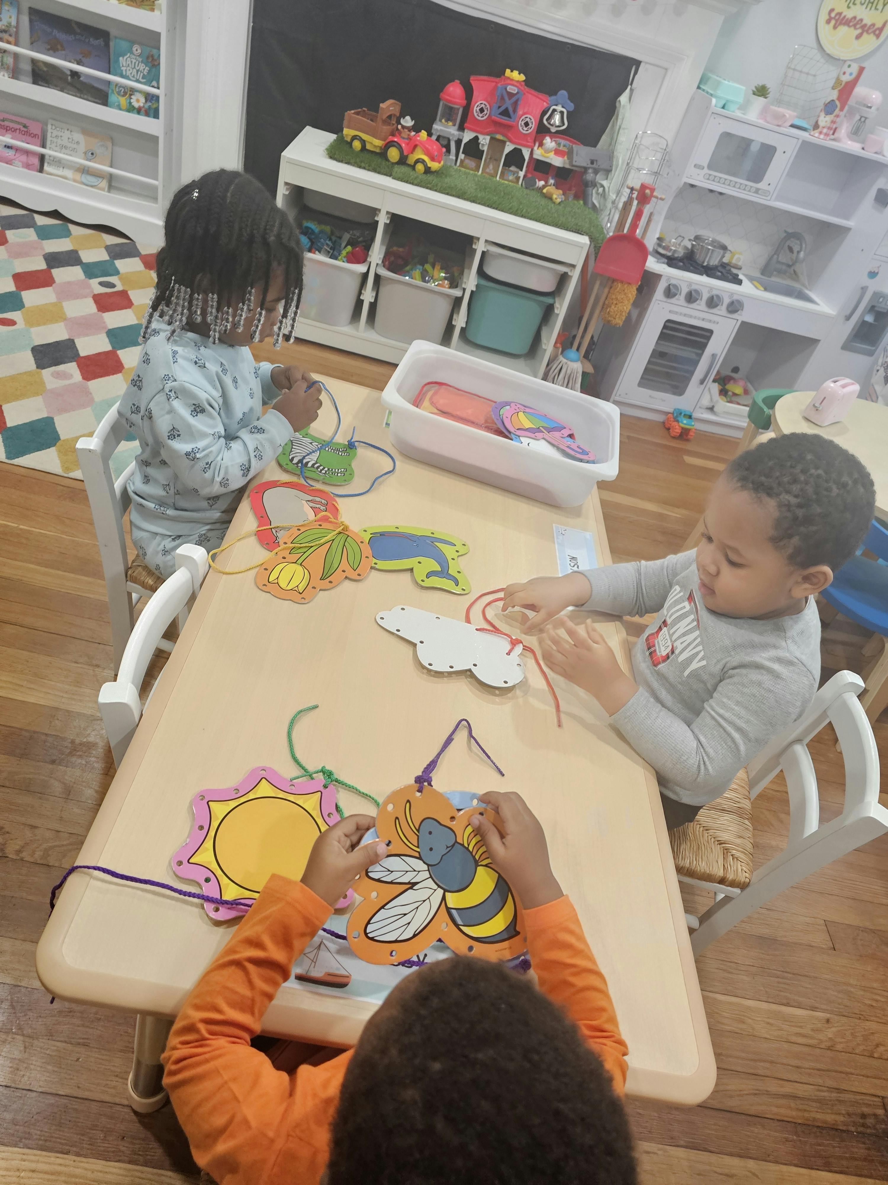 Three children sitting at a table doing a lacing activity