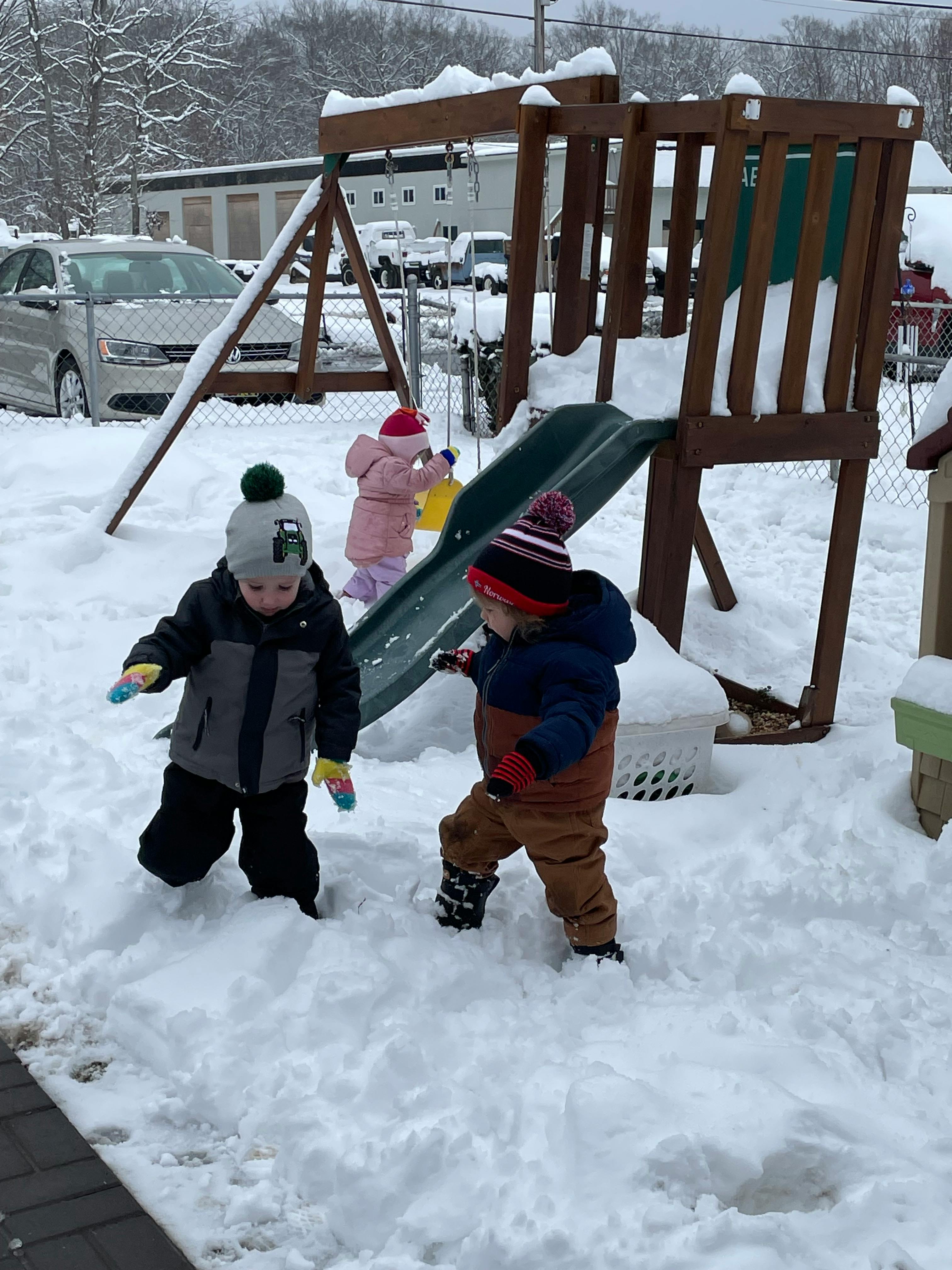 Three children playing in the snow near a playground set