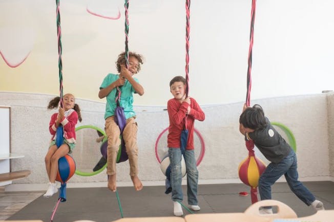 Four children playing on hanging ropes with punching bags