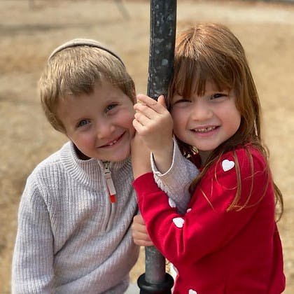 Two children smiling and leaning on a pole