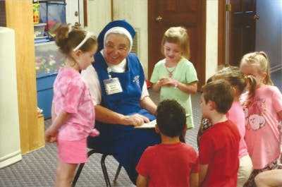 Person in blue habit reading to a group of children