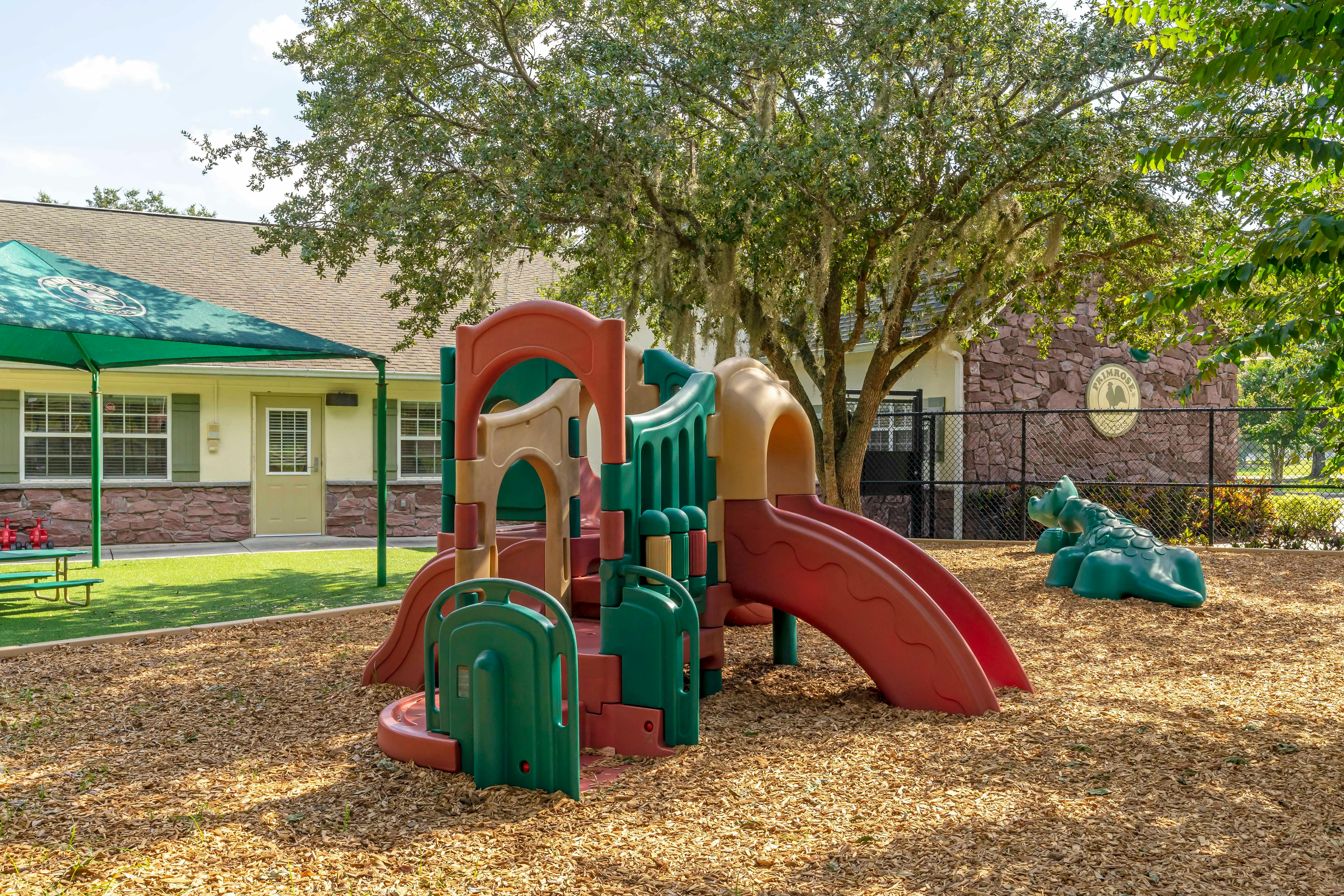 Colorful playground structure with slides on wood chip ground, building in background
