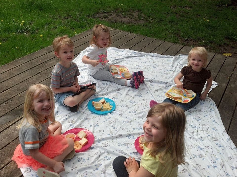 Five children sitting on a blanket outdoors with plates of food