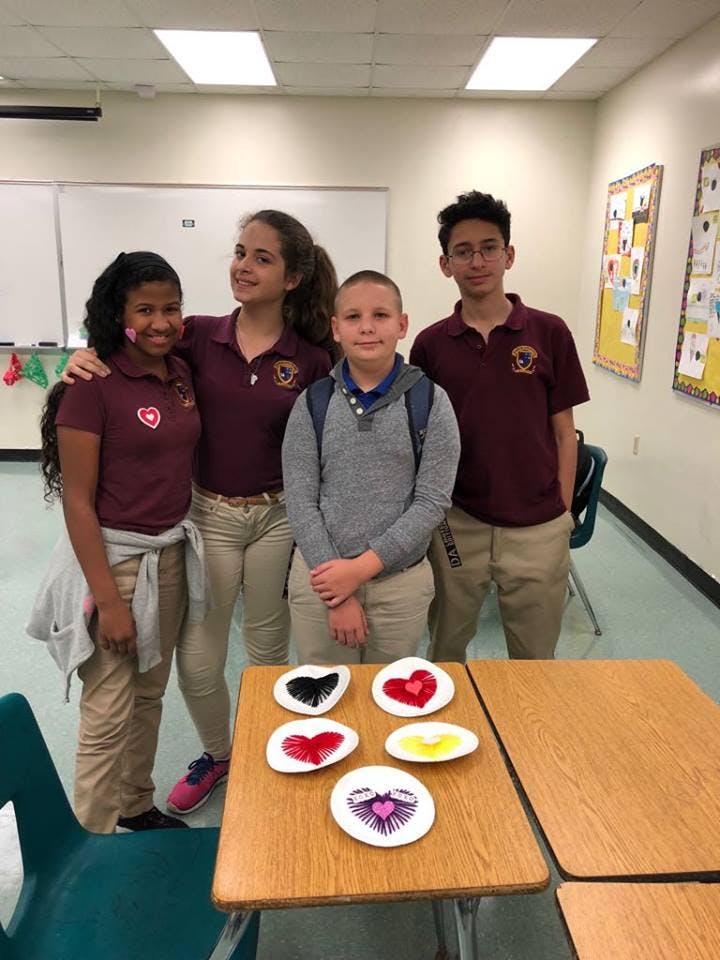 Four teens and children standing in a classroom with heart-shaped crafts on a desk
