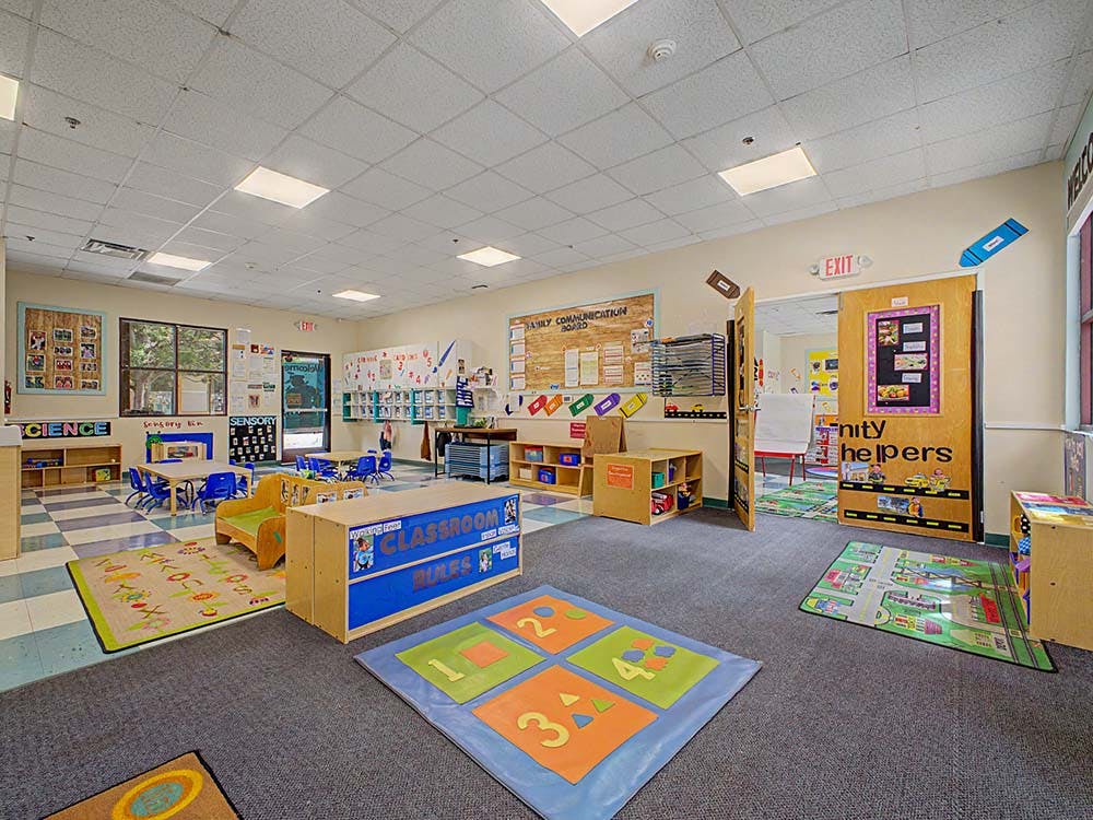 Empty classroom with small tables and chairs, play mats, and learning displays
