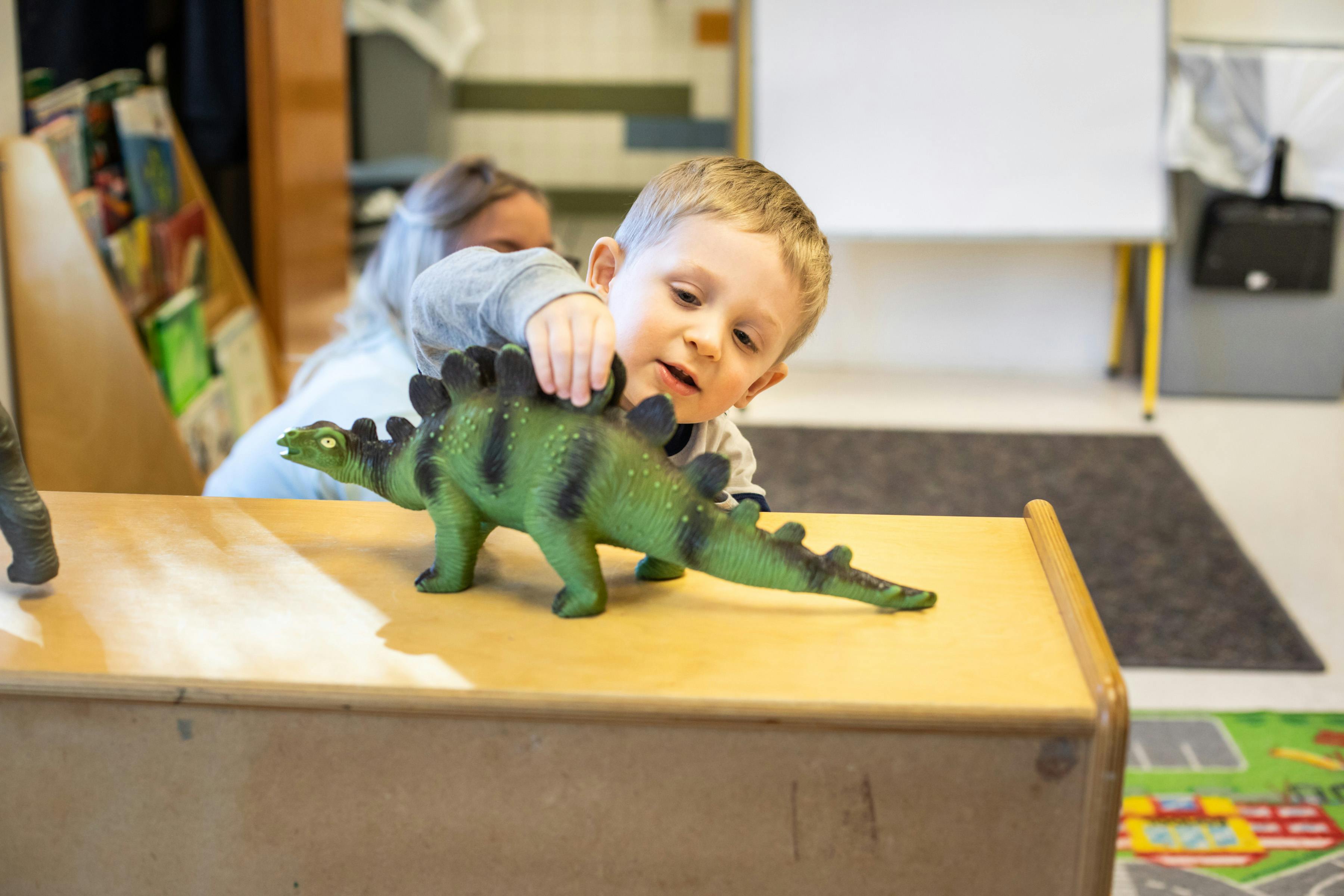 Child playing with a green dinosaur toy